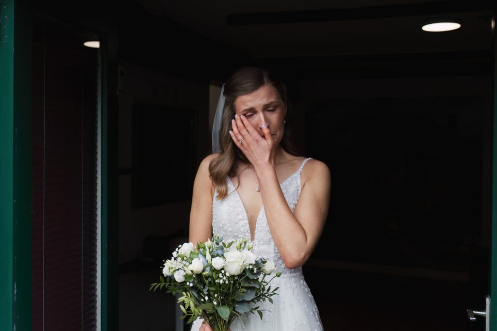 A documentary-style capture of a bride crying while waiting for her dad for the first look.